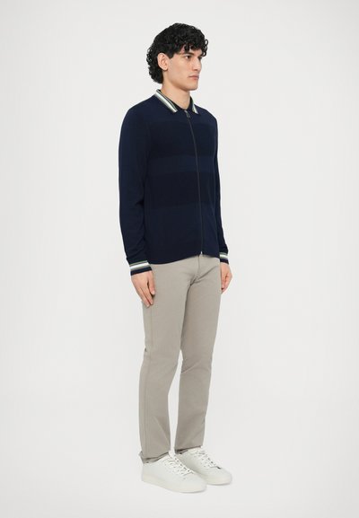 Tmavomodrý kardigán na zips s pruhovaným golierom a textúrovaným vzorom. Kombinovaný s svetlosivými nohavicami a bielymi teniskami. Minimalistický štýl.