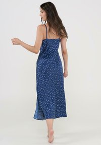 Vestido maxi sin mangas de color azul marino con un patrón de estrellas blancas, que presenta aberturas laterales y una tela suave, mostrando un corsé ajustado y una falda fluida.