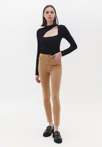 Sort langærmet bluse med firkantet udsnit, parret med tætsiddende tan jeans og sorte platform sko med et gult accent.