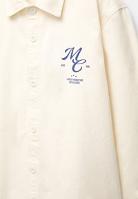 Cream button-up shirt with blue "MC EST. 1991 LUXE ET PRESTIGE CÔTE D'AZUR" text and star graphic on the left chest.