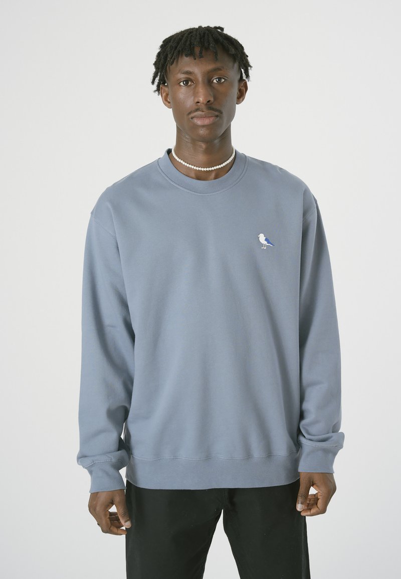 Helles blaues Sweatshirt mit langen Ärmeln, Rundhalsausschnitt und kleinem Vogel-Logo auf der Brust. Weicher Stoff, lockere Passform und gerippte Bündchen.
