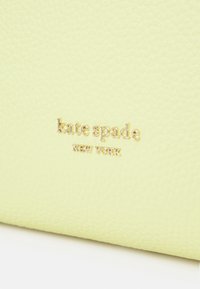 Cuero amarillo texturizado con un logo en relieve que dice "kate spade NEW YORK" en dorado, posicionado de forma central en la superficie.