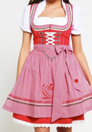 Kvinde iført en traditionel rød og lyserød ternet dirndl-kjole med hvid bluse og hjertebroderi på forklædet.