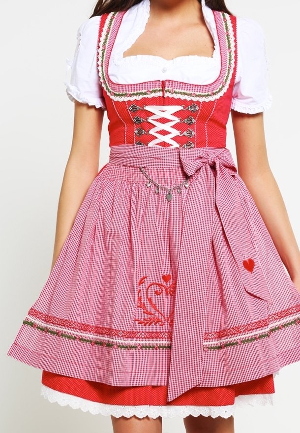 Femme portant une robe dirndl traditionnelle à carreaux rouges et roses avec une blouse blanche et une broderie en forme de cœur sur le tablier.