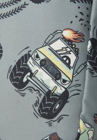 Tyget har en grå bakgrund med tecknad stil på monstertrucks, gummidäck, lågor och färgglada geometriska mönster.
