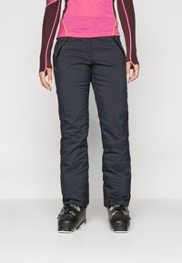 Pantaloni da sci neri isolati con una superficie liscia, tasche laterali e un design attillato. Indossati con stivali da sci neri per l'uso all'aperto.