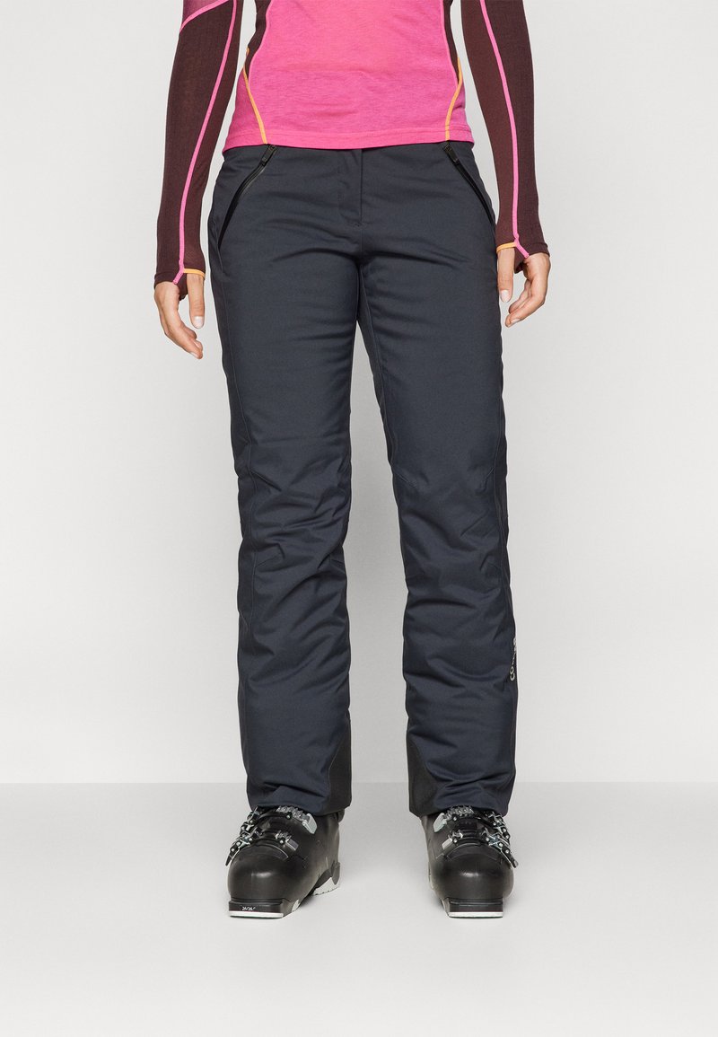 Pantaloni da sci neri isolati con una superficie liscia, tasche laterali e un design attillato. Indossati con stivali da sci neri per l'uso all'aperto.