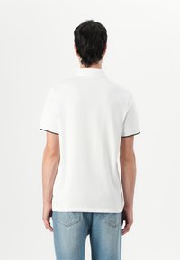 Witte polo met korte mouwen en kraag, met zwarte accenten op de mouwen, gecombineerd met lichtblauwe spijkerbroek. Eenvoudig, klassiek ontwerp.