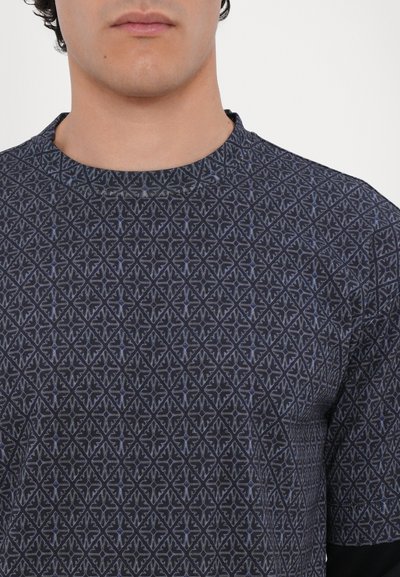 Īsām piedurknēm, tumši rakstaina T-krekla, kas izceļ ģeometrisku dizainu zilās un pelēkās krāsās, ar apaļu kakla izgriezumu un mīkstu tekstūru.