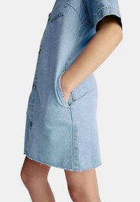 Jeanskleid in Hellblau, mit kurzen Ärmeln, Knopfleiste und Seitentaschen. Rohkante am unteren Ende sorgt für Textur.