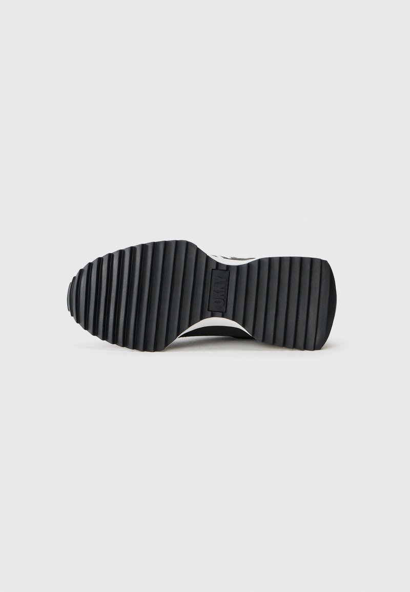 Semelle de sneaker noire avec des rainures horizontales et un motif texturé, présentant un accent blanc et un détail de logo au centre.