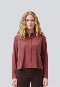 Maroon button-up shirt with long sleeves, soft texture, and a relaxed fit, paired with dark brown corduroy pants. Plain background.