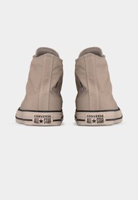 Ζευγάρι μπεζ ψηλά παπούτσια Converse All Star, εμφανιζόμενα από πίσω σε λευκό φόντο.