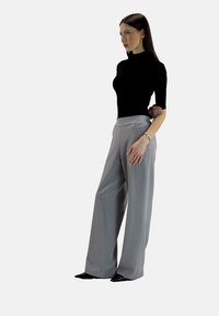 Top aderente nero e pantaloni grigi a vita alta a gamba larga. Tessuto morbido con un leggero lucido; silhouette elegante; lunghezza alla caviglia. Scarpe nere.