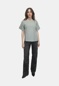 Top a righe verde e bianco con maniche corte, abbinato a pantaloni in denim scuro a vita alta. Il top presenta una forma quadrata e una vestibilità rilassata.