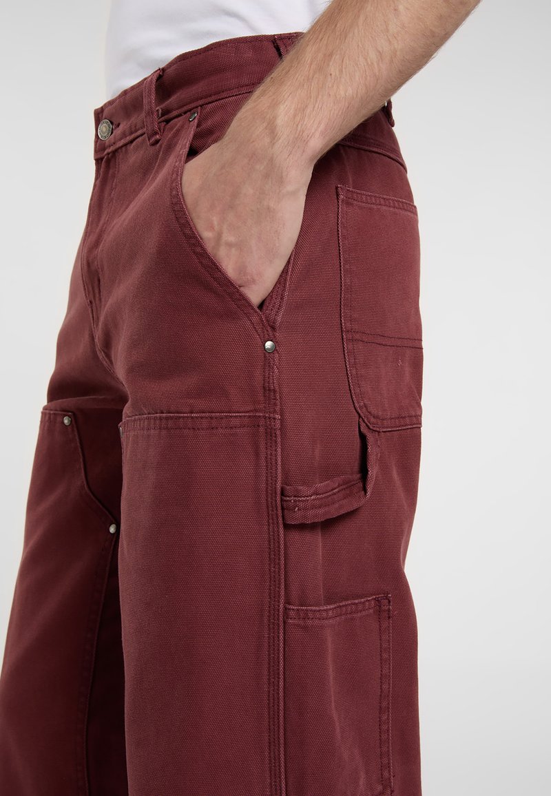 Bordeaux arbejdsbukser lavet af robust stof; har sidelommer, sølvhardware og en afslappet pasform med synlige syninger.