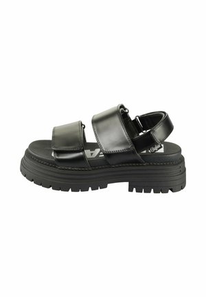 Sandale noire à semelle épaisse avec deux larges bandes velcro sur le dessus du pied et une autour du talon sur fond blanc.