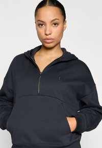 Σκούρος γκρι φούτερ με κουκούλα από απαλό υλικό, διαθέτει κλείσιμο με φερμουάρ τριών τετάρτων, μεγάλη μπροστινή τσέπη και μανσέτες με ριμπ ύφανση. Περιλαμβάνει διακριτικό λογότυπο.