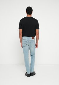 Černé tričko s krátkým rukávem spojené se světle modrými džínami. Džíny mají na zadní straně hnědou koženou nášivku a úzký střih.