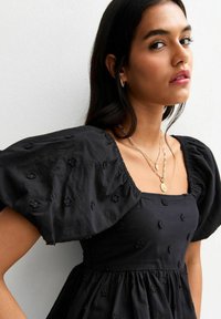 Black embroidered dress featuring puffed sleeves, square neckline, and detailed floral patterns. The fabric appears soft and textured.