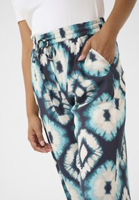 Elastne vöökoht ja sidumismuster, kus on sinise ja kreemika värvi toone. Valmistatud kergest kangast, millel on funktsionaalsed taskud.