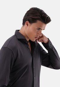 Camicia button-up grigio scuro con colletto alla francese e maniche lunghe, caratterizzata da una texture sottile e bottoni abbinati, indossata da un modello.