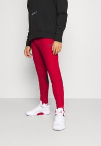 Pantalones deportivos rojos con detalles en negro y logo de Jordan, combinados con zapatillas blancas con detalles rojos y tejido texturizado. Sudadera con capucha negra.
