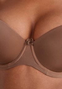 Beha van zacht, matbruin stof met gevormde cups en een centrale strikaccent. Heeft soepele randen en een naadloos ontwerp voor comfort.