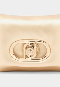 Beige læder clutch med glat tekstur, der har en guldfarvet metallogo detalje og en oval accent foran.