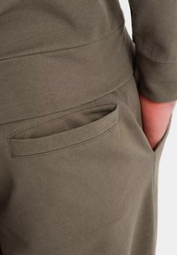 Joggers de mezcla de algodón verde oliva con un bolsillo lateral, textura suave y diseño de corte relajado. Detalle de costura por encima del bolsillo.