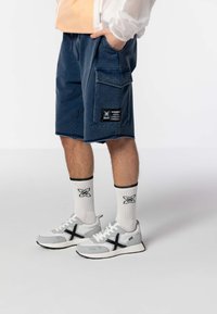 Shorts de mezclilla en azul marino con bolsillos laterales y una etiqueta. Zapatillas grises con acentos negros, combinadas con calcetines blancos que tienen un logo negro.