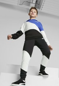 Kindertrainingsanzug in Blau, Schwarz und Weiß. Verfügt über ein farbblockiertes Design mit Kapuze, elastischem Bund und gerippten Manschetten. Schwarze Sneakers.