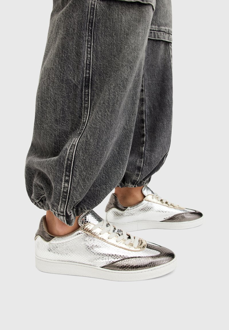 Metallic silver sneakers with a textured finish and contrasting dark accents, paired with gray elastic cuffed pants.