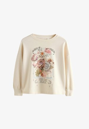 Šviesiai smėlinis megztinis su ilgomis rankovėmis, su gėlių dizainu ir užrašu "TU ESI MAGIJA" spausdintu centre. Minkšta tekstūra.