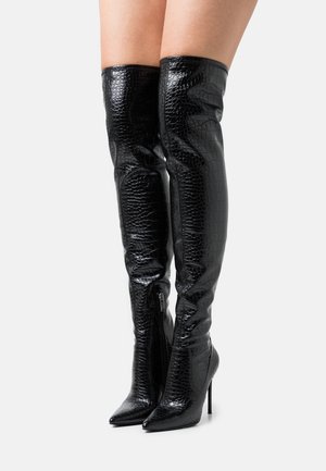 Bottes noires au-dessus du genou en matière vernie embossée façon croco, avec un bout pointu et un talon aiguille. Fermeture éclair latérale incluse.