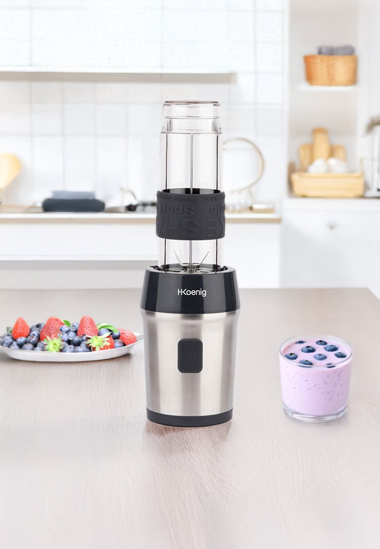 Mixeur en acier inoxydable avec une base et un couvercle en plastique noir. Bol de mélange transparent avec une prise en caoutchouc, doté de lames aiguisées à l'intérieur.