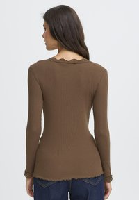 Brun langærmet top lavet af ribbet stof med bølget blonder langs udskæringen og ærmerne. Tæt siddende design med en rund nederkant.
