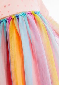 Rosa klänning med prickar och en lager på lager tullekjol i regnbågens färger, med ljusblå, rosa, orange och gula genomskinliga paneler.