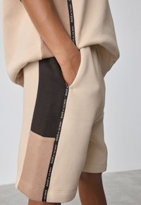 Beige jerseynederdel med farveblok-design i sort og tan sektioner. Inkluderer en sidelomme og en kontrasterende mærkebetegnelse.