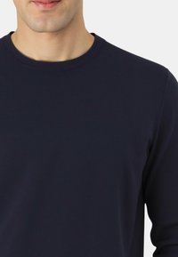 Maglietta a maniche lunghe blu navy con collo rotondo a costine, dalla texture liscia, caratterizzata da un design aderente e cuciture sottili lungo le cuciture.