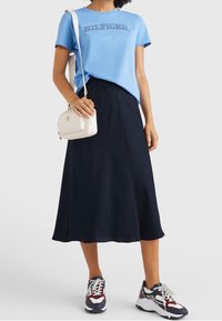 Camiseta de algodón azul claro con el logo "HILFIGER", combinada con una falda midi azul marino, un bolso cruzado blanco y zapatillas deportivas coloridas.