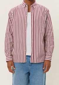 Chemise rayée à boutons rouge et blanche, en tissu léger, avec col pointu et une poche poitrine. Manches longues avec détails aux poignets.