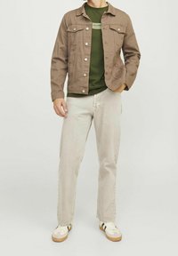 Chaqueta de mezclilla marrón, camiseta verde, jeans gris claro y zapatillas beige. Los detalles notables incluyen botones de metal y dos bolsillos en el pecho.