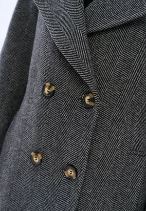 Grijs visgraat patroon dubbelbreasted jasje met piekflappen, voorzien van zwarte knopen met gouden accenten.