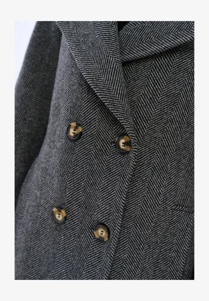Szary żakiet w jodełkę, podwójnie zapinany, z ostro zakończonym kołnierzem, z czarnymi guzikami z złotymi akcentami.
