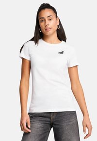 Hvid bomulds t-shirt med rund halsudskæring, korte ærmer og et sort Puma-logo på venstre bryst. Bæres med mørke denim jeans.