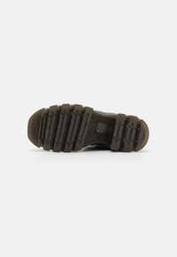 Suola nera di scarpe da ginnastica realizzata in gomma testurizzata con modelli di battistrada profondi, scanalature e segni di usura, progettata per aderire e durare nel tempo.