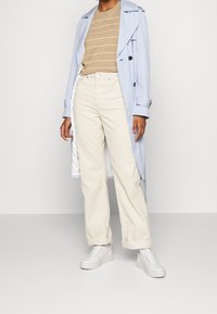 Lyseblå trenchcoat, tan stribet sweater, hvide corduroy bukser og hvide sneakers. Har dobbeltrindet front og oprettede ærmer.