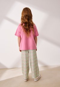 T-shirt rose à manches courtes associée à un pantalon vert à motif floral à jambes larges et des baskets blanches, vue de dos.