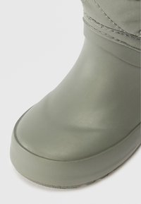 Botte verte imperméable en caoutchouc, dotée d'une texture lisse et d'un bout arrondi. La tige a un accent en tissu avec des détails cousus.